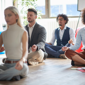 Group of people meditating in a modern office setting, that is kitted out as a wellness space